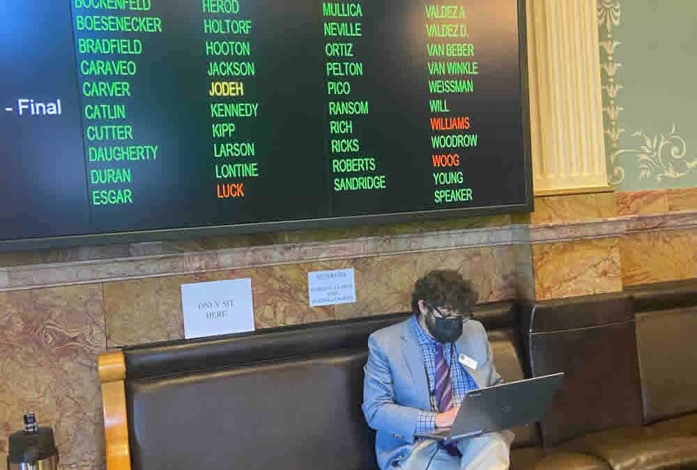 Man sitting on bench with billboard in background with voting results for HB21-1279.